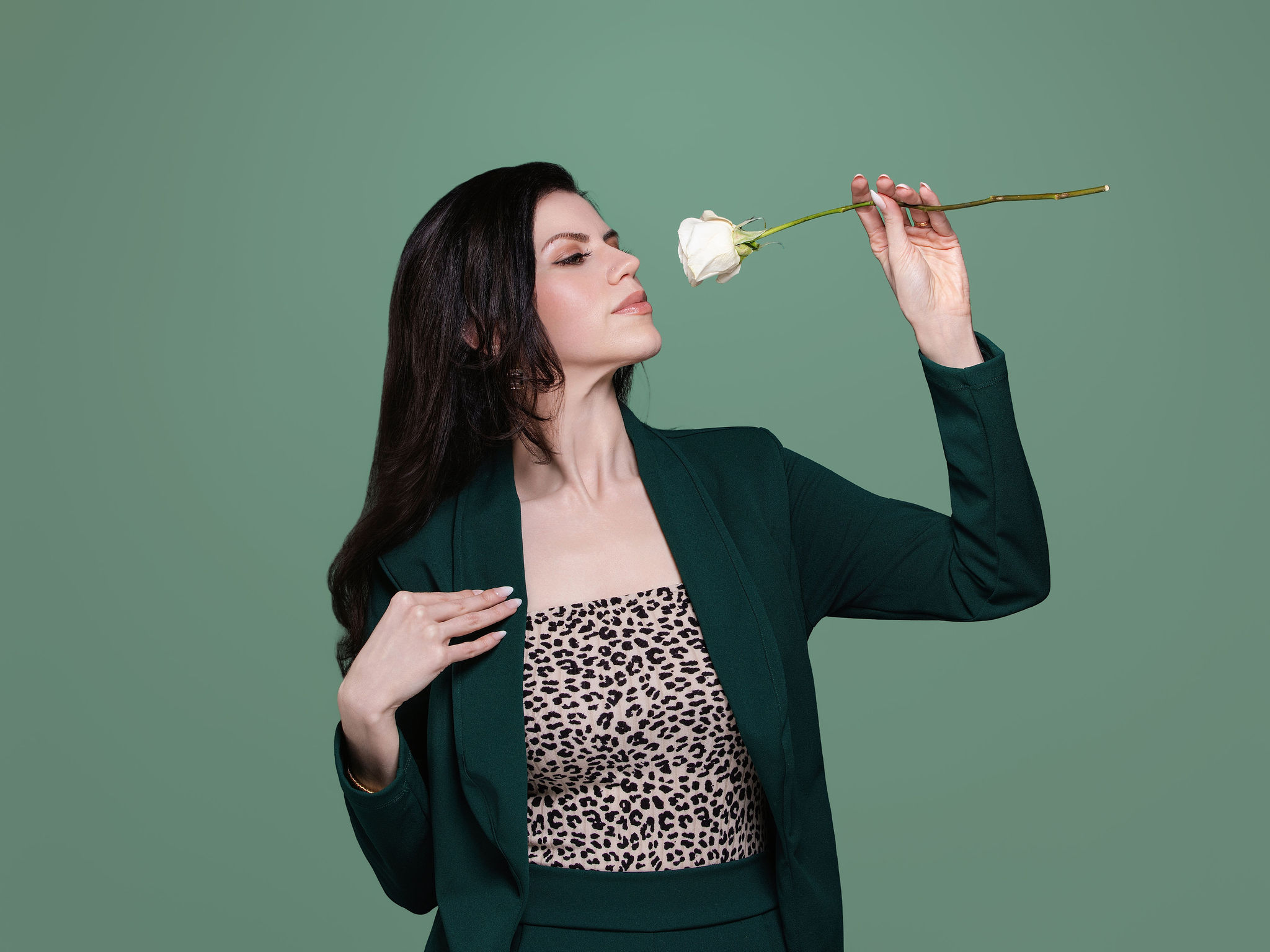 Meggan smelling a white rose against a sage-green backdrop